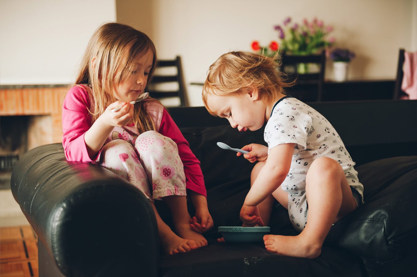 Two young children eat breakfast in pajamas