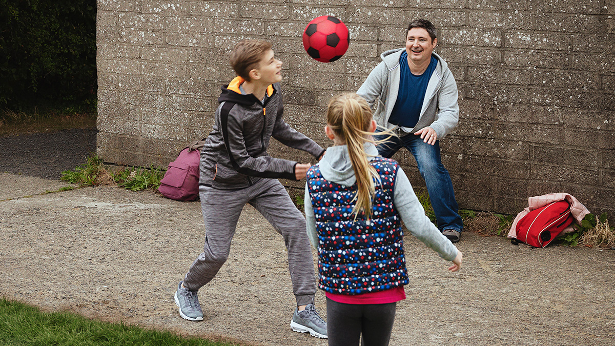 A dad playing football with his son and daughter