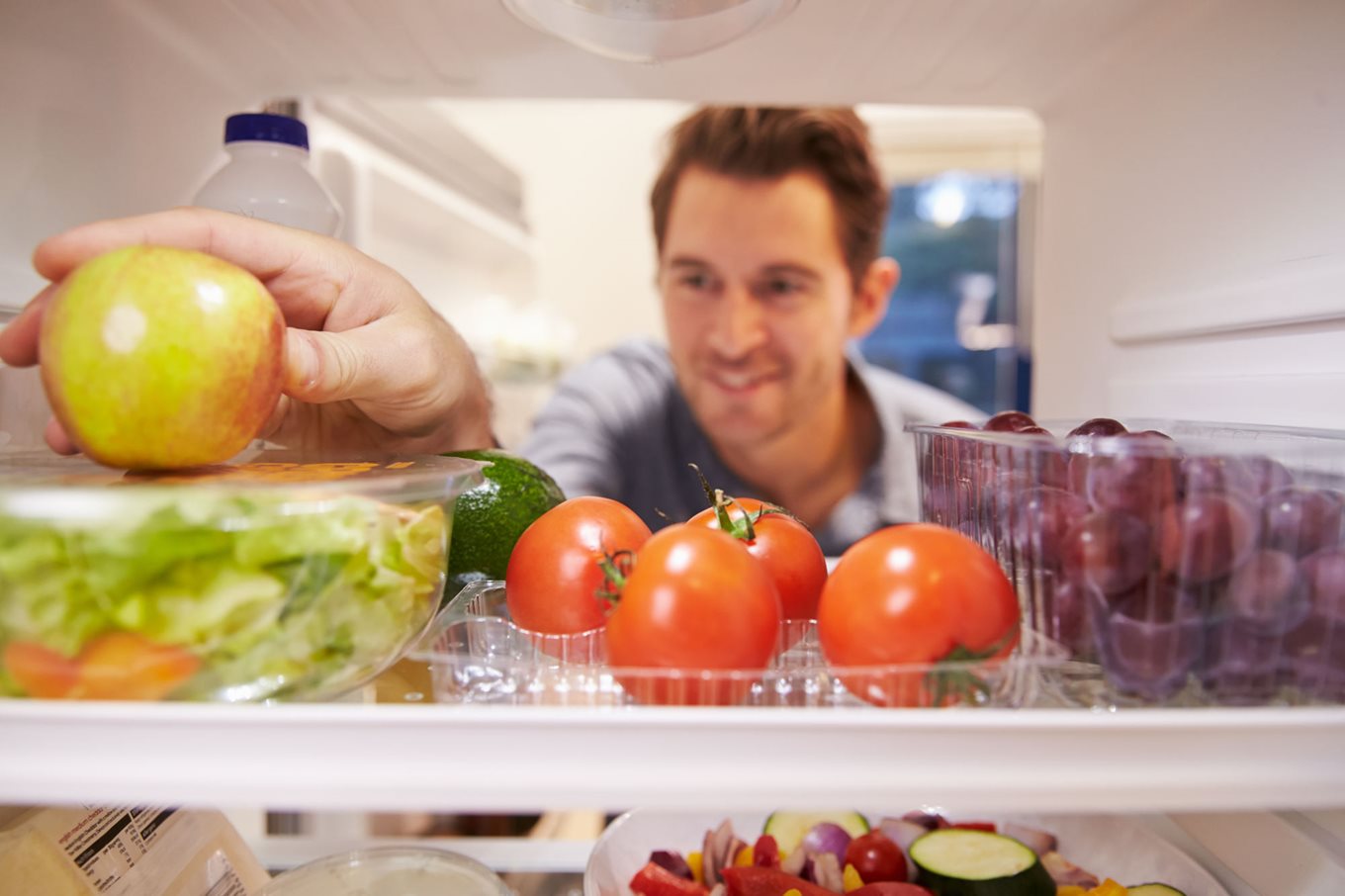 A man reaches into the fridge for an apple