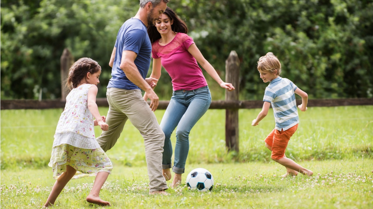 A dad playing football with his son and daughter
