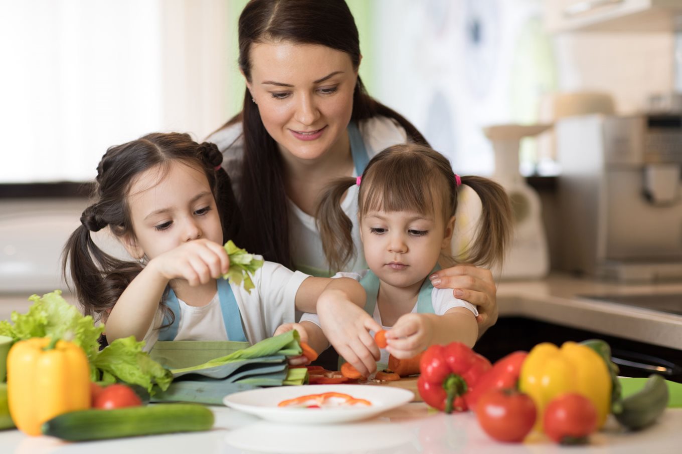 Woman helping two children make a salad