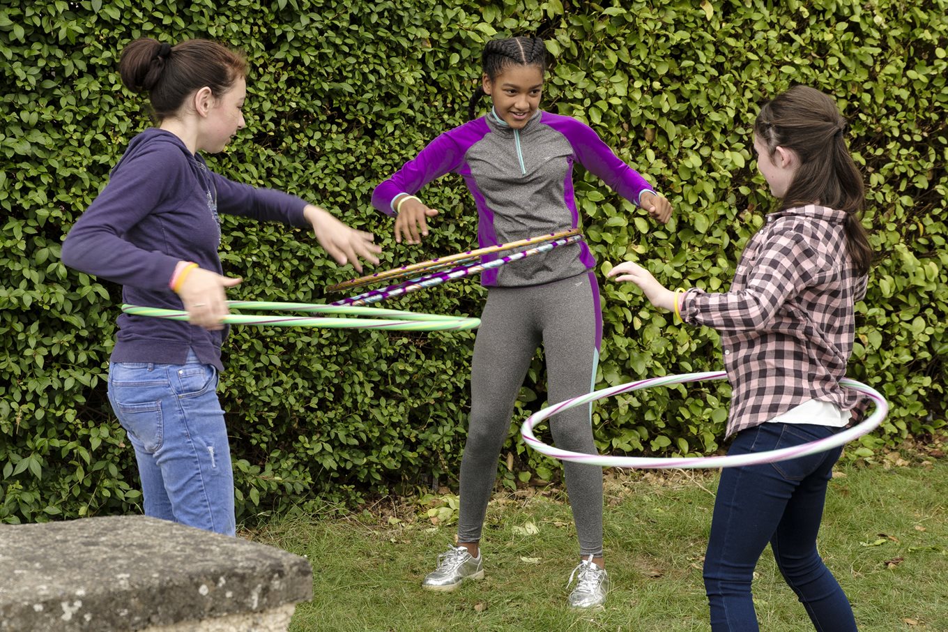 Three girls play with hula hoops in the garden