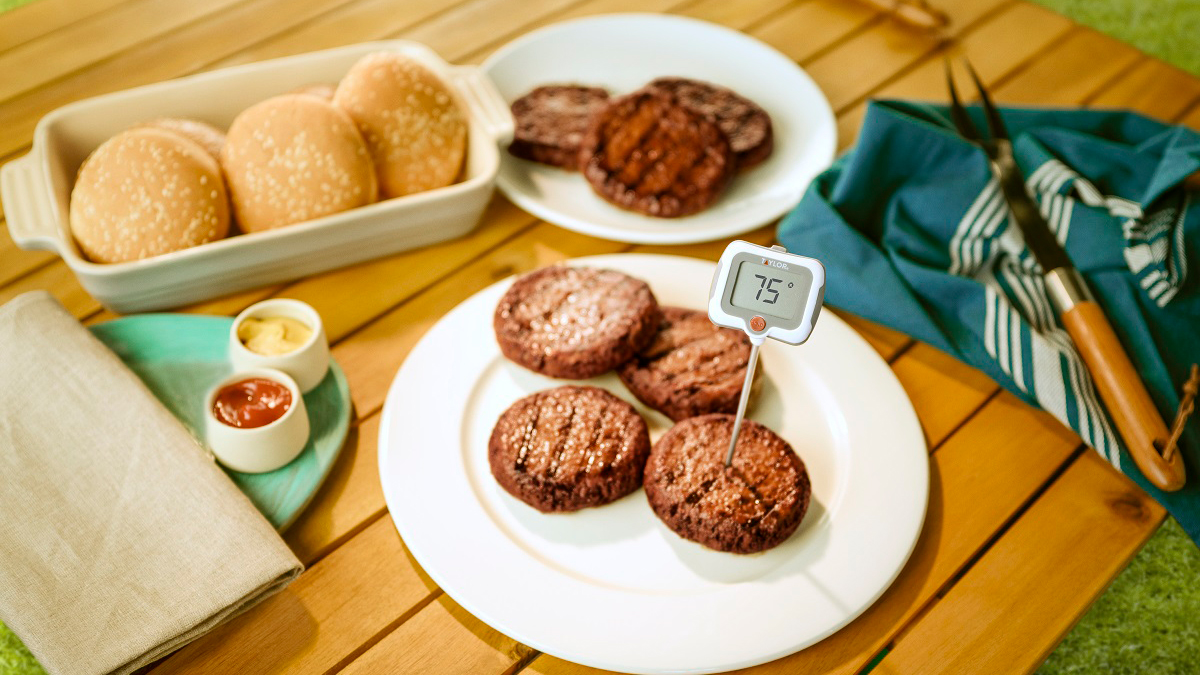 Burgers on an outside table with a meat thermometer reading 75 degrees