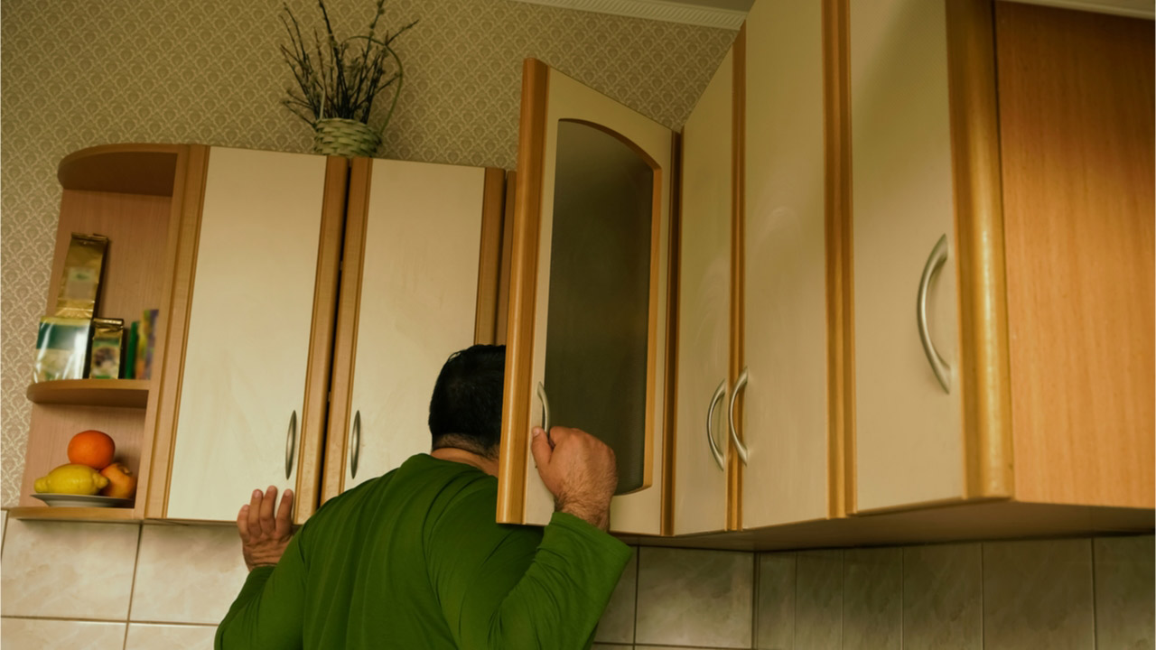 A man searches kitchen cupboards