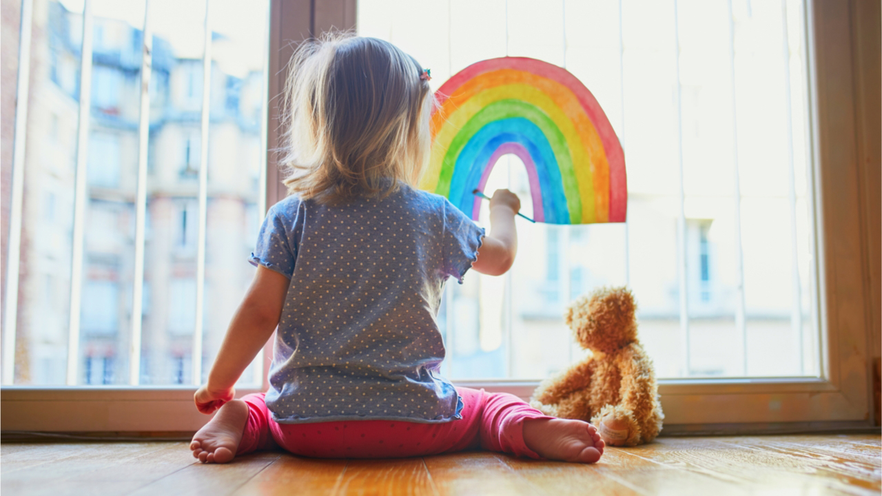 Little girl painting a rainbow on the window