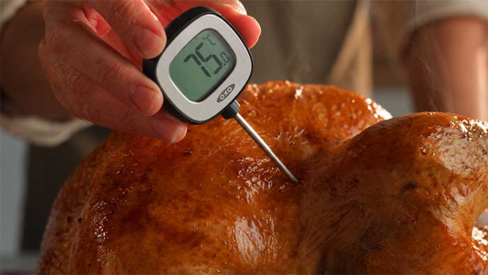 Meat thermometer probe inserted between the breast and the leg of a whole turkey